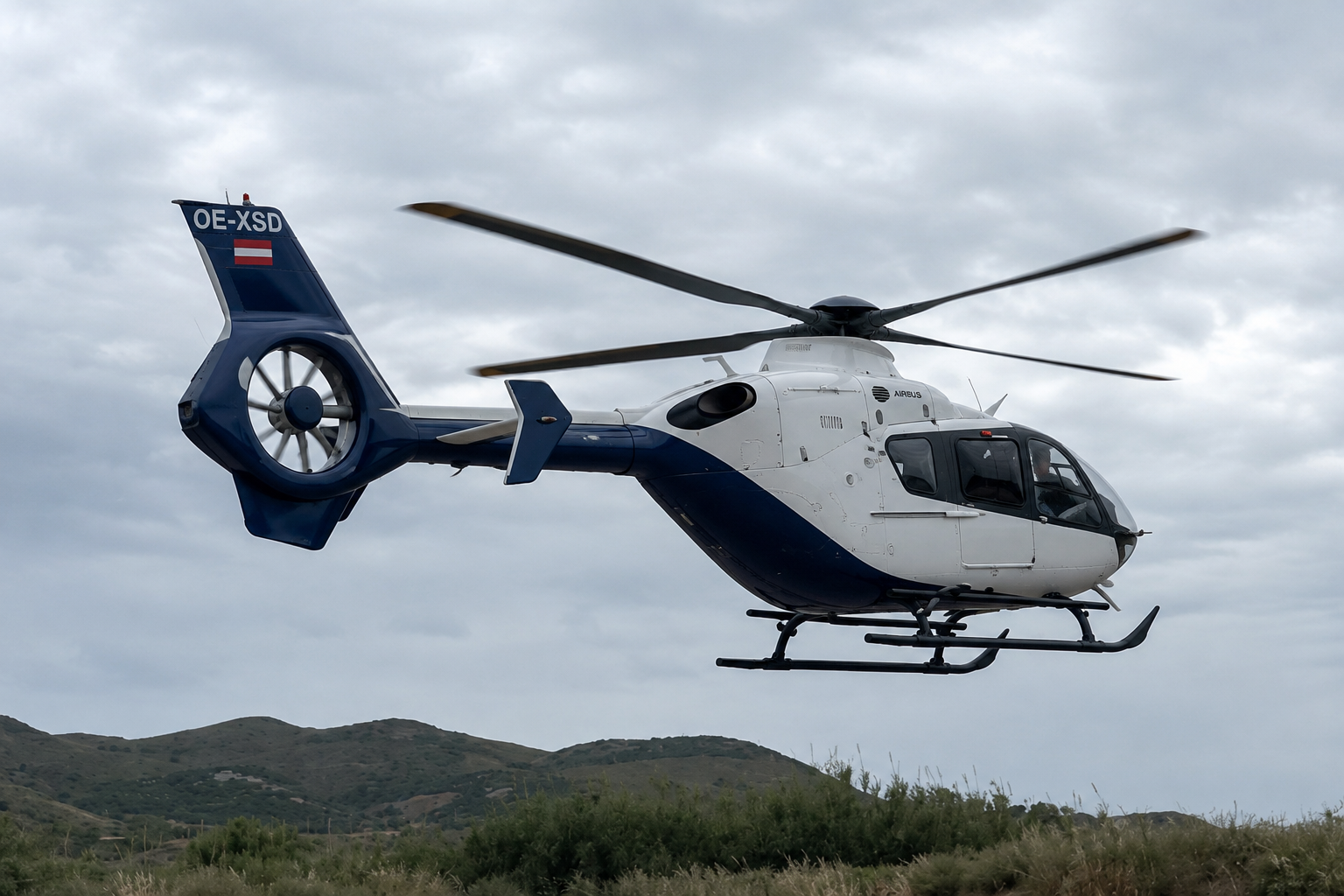 Airbus H135 helicopter flying over the Greek landscape during cloudy weather conditions for Fly G Aviation operations in Greece