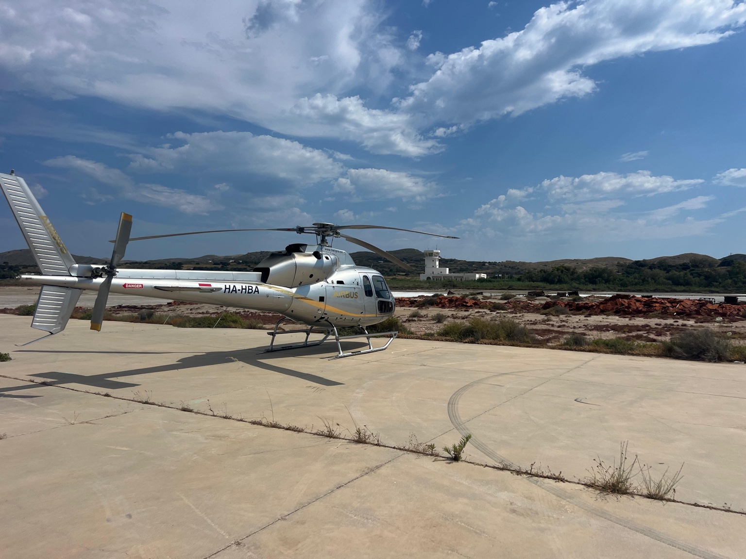 Airbus H135 helicopter at Alykes landing point in Milos, Greece, arriving for a private helicopter transfer on a summer day.